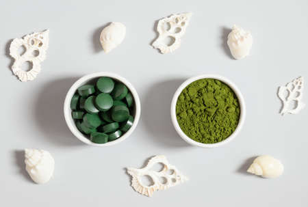 Chlorella and spirulina on a gray background with seashells. Chlorella powder and spirulina tablets. Detox superfood. natural supplement of algae. Top view, flat lay.の写真素材