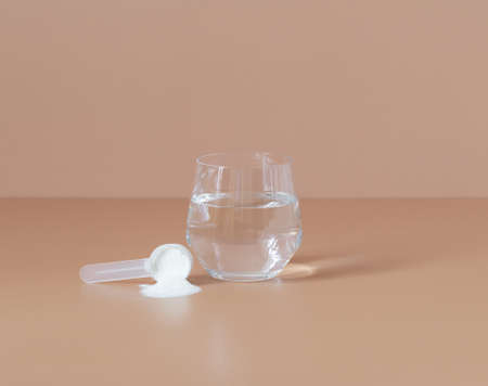 Collagen. Measuring spoon with collagen powder or protein and water on a beige background. natural...