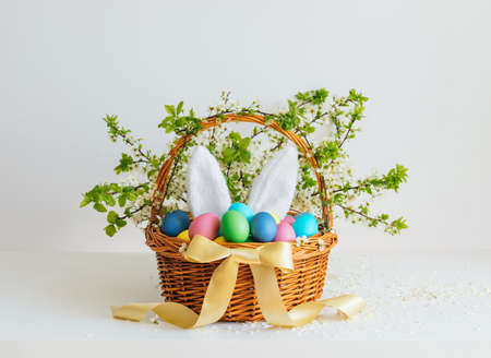 Easter basket with eggs and bunny ears on a white background. Beautiful Easter composition. Festive...