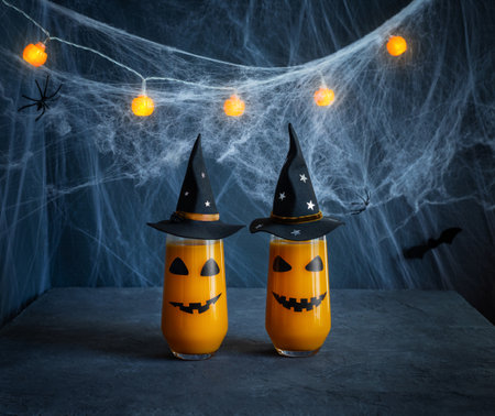 Halloween pumpkin cocktail on a dark blue background in a spider web. Glasses with jack lantern face in black witch hats. Halloween drink. copyspace.の写真素材