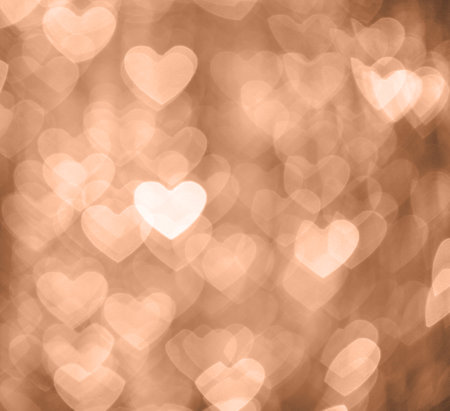 Peach Fuzz abstract bokeh background in the shape of hearts. Color of 2024 year Peach Fuzz. Defocused shiny sequins.の写真素材