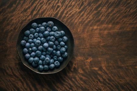 Ripe blue blueberries in a dark plate on wooden background with copy space. Fresh blue berries in a bowl. Top view, flat lay.の写真素材