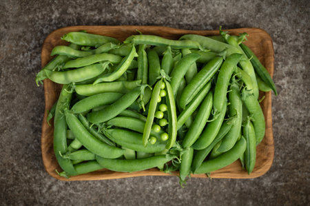 Green peas in a wooden plate on a dark background. Fresh green peas in pods. Top view, flat lay.の写真素材
