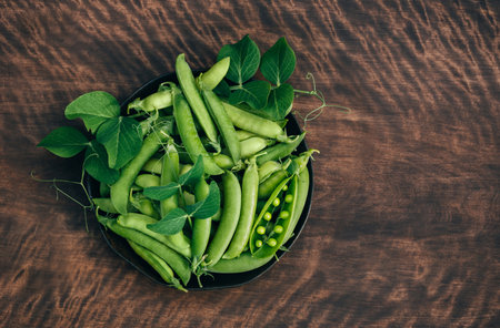 Green peas with pods and leaves in a bowl on wooden background with copy space. Organic vegetables....