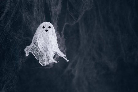 Funny ghost made of gauze and starch on dark spider web background with copy space. Creative DIY Halloween decor.の写真素材