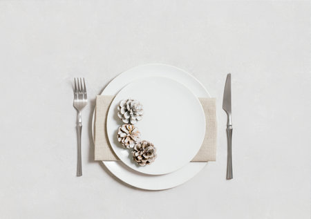 Table setting with silverware, napkin, cones and a white plate on a white background. Christmas or New Year dinner. Copy space. Top view, flat lay.の写真素材
