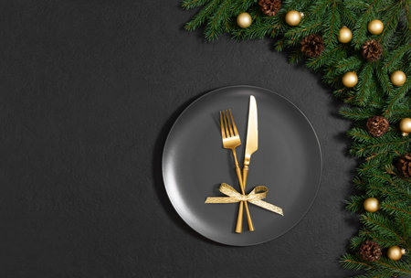Christmas festive table setting on a black background. Black plate, gold cutlery and fir branches with decorations for New Year's Eve dinner. Copy space. Top view, flat lay.の写真素材