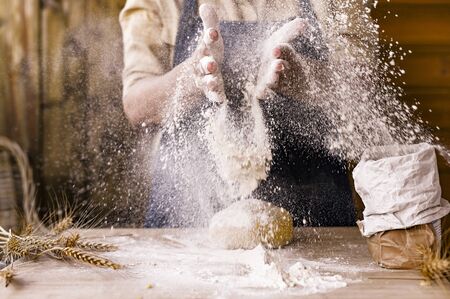 Women's hands, flour and dough. Levitation in a frame of dough and flour. A woman in an apron is preparing dough for home baking. Rustic style photo. Wooden table, wheat ears and flou.Emotional photoの写真素材