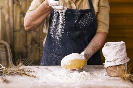 Women&#39;s hands, flour and dough. Levitation in a frame of dough and flour. A woman in an apron is preparing dough for home baking. Rustic style photo. Wooden table, wheat ears and flou.Emotional photoの写真素材