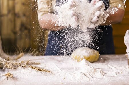 Women's hands, flour and dough. Levitation in a frame of dough and flour. A woman in an apron is preparing dough for home baking. Rustic style photo. Wooden table, wheat ears and flou.Emotional photoの写真素材