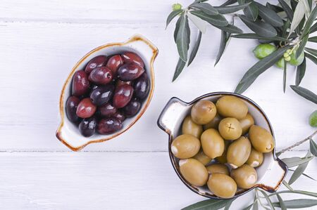 Traditional appetizers, olives from Greek cuisine. White wood background. View from above. Fresh branches of olives. Copy spaceの写真素材