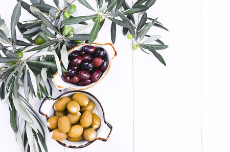 Traditional appetizers, green and red olives from Greek cuisine. White wood background. Fresh branches of olives. Copy spaceの写真素材
