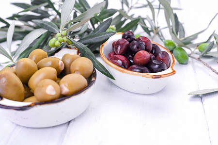 Traditional appetizers, green and red olives from Greek cuisine. White wood background. Fresh branches of olives. Copy spaceの写真素材