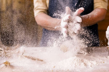 Womens hands, flour and dough. Levitation in a frame of dough and flour. A woman in an apron is preparing dough for home baking. Rustic style photo. Wooden table, wheat ears and flou.Emotional photoの写真素材