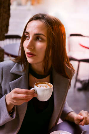 Beautiful young girl is drinking coffee in a street cafe. Bologna, Italy. Traditional italian espresso coffee in womans hands close-up. Toned photo, soft selective focus. art processing.の写真素材