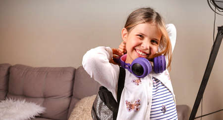 Little girl in musical headphones and a backpack is ready to go to school. A European schoolgirl...
