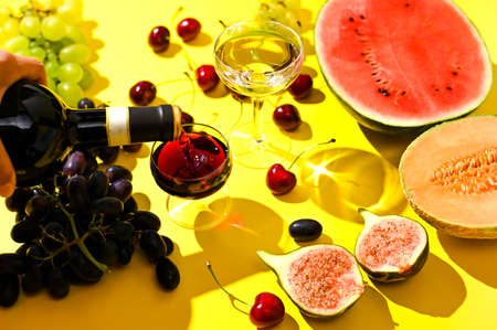 Two glasses of red and white wine. A woman pours wine from a bottle. Grapes and other fruits on a yellow background. The concept of harvest and Italian winemakingの写真素材