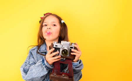 Little girl with a retro camera on a yellow background. The child shows happy emotions and poses. Tourism concept. Copy space.の写真素材