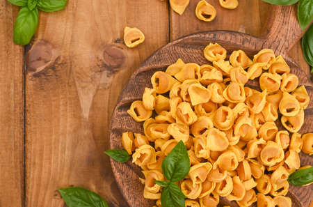 Tortellini mignon on a wooden board with basil and parmesan. Specialties of the cuisine from Bologna and Emilia Romagna: Cappelletti, fresh egg pasta with meat and vegetables filling. Copy spaceの写真素材