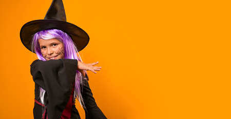 Enthusiastic little girl in a witch costume . Person posing on a yellow background in the studio....
