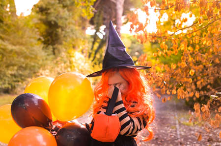 Sad Child in a carnival costume on Halloween with large colored balloons. Little girl in the autumn...