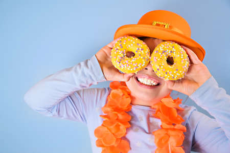 Kings Day in Holland. Traditional festival on April 27 in the Netherlands. A little girl in a festive orange hat holds in hands colored donuts. Copy spaceの写真素材