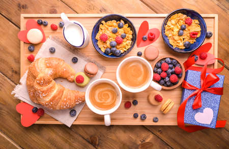 Sweet surprise in Valentines Day. Breakfast for a couple of lovers. Aromatic coffee, muesli with berries and sweet pastries on a wooden table. Above. High quality photoの写真素材