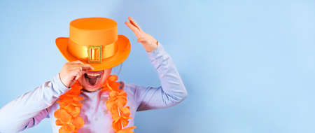 Kings Day in Holland in the spring. Traditional festival on April 27 in the Netherlands. Little girl in a festive orange hat on a blue background eats colored donuts. Banner, long format. Copy spaceの写真素材
