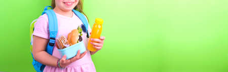 Young schoolgirl with lunch box on a green background. Little girl with a school backpack and a set...