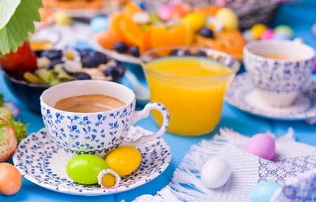 Easter breakfast. Fresh aromatic espresso coffee and easter colored eggs on a blue wooden background. Muesli, strawberries for breakfastの写真素材