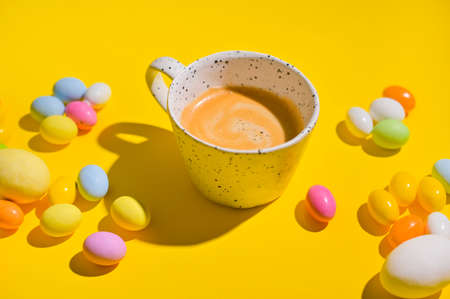 A lot of multi-colored Easter eggs and a mug of coffee with froth on a yellow background. Happy Easter card with copy space for text. Minimal style. In a hard light. selective focusの写真素材