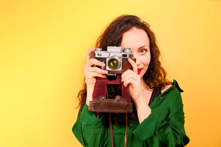A person holding a camera. Fashion portrait woman holds retro camera on a yellow background. In bright colors, free space for text. High quality photoの写真素材
