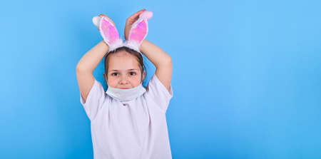 A child in a protective medical mask and decorative rabbit ears holds Easter eggs in his hands. World pandemic  2019 2020. Copy space . Banner long formatの写真素材