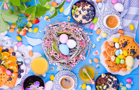 Easter breakfast scene shot from above. Cups for tea, cake with jam, cookies, fresh orange juice, fruits, granola with berries, honey, strawberries with leaves and berriesの写真素材