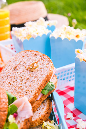 Lunch in the park on the green grass. Summer sunny day and picnic basket. Popcorn and sandwiches for a snack outdoors in nature. in bright plastic dishes . Verticalの写真素材
