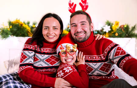 Happy family in christmas posing in red sweaters. Celebrating new year and christmas at home in 2021. Mom, dad and little daughter are having fun. High quality photoの写真素材