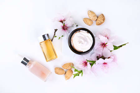 Jar with cream, oil and essence on a light background. Hand care lotion with almond oil and vitamins. Body skin health and beauty. Cosmetics and natural almond flowers. Copy space . Mockupの写真素材