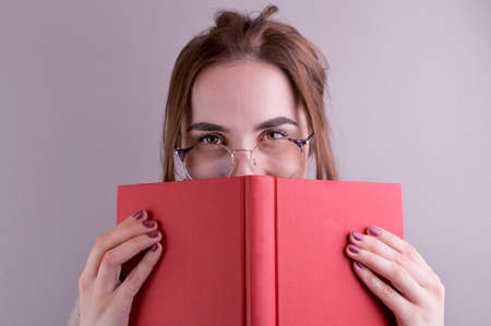 A young girl in glasses is reading a book. woman on a gray background. The concept of education and information. Free space for textの写真素材