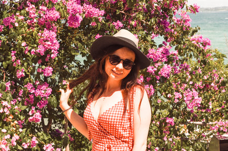 girl in a hat near a large bush with pink flowers. Aged photo with tintingの写真素材