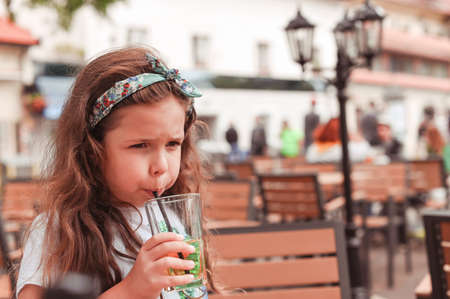 Little girl in a cafe on the street drinks juiceの写真素材