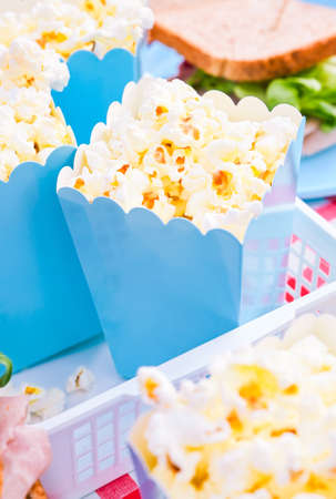 Popcorn and sandwiches for a snack outdoors in nature. in bright plastic dishes . Lunch in the park on the green grass. Summer sunny day and picnic basket. FullHD footage, Slow motionの写真素材