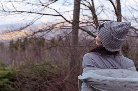 A girl in a hat and jacket stands on a panorama overlooking the hills and the village. Tourism and travel concept. Copy space.の写真素材