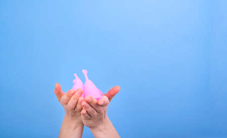 Woman holds different menstrual cups in her hands on a blue background. Women health concept, zero...