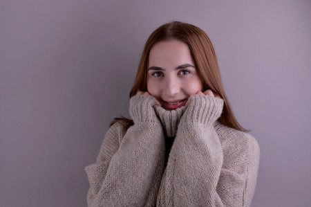 Beautiful smiling girl in a sweater on a gray background. Studio shot. Modern portrait. Copy space