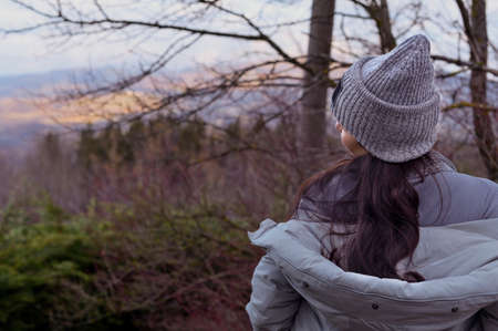 A girl in a hat and jacket stands on a panorama in the forest, the sky is a tree. Tourism and travel concept. Copy spaceの写真素材