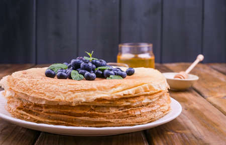 Pancakes with blueberries and honey on a plate, on wooden roofing. Traditional pastries for the Russian festival of Maslenitsa. free space for text.の写真素材