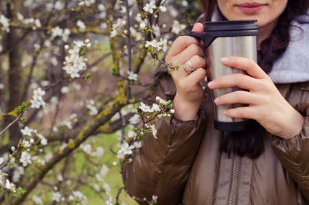 Girl with a coffee or tea mug in the garden of flowering trees in spring. Break, walk and relax in...
