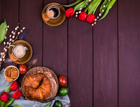 Easter breakfast with aromatic fresh espresso, croissants, colored eggs, red tulips and willow. Coffee with pastries, flowers on a wooden table. View from above. Copy spaceの写真素材