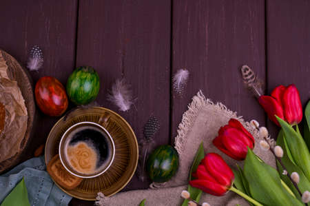 Easter breakfast with aromatic fresh espresso, croissants, brownie cake, colored eggs, red tulips and willow. Coffee with pastries, flowers on a wooden table. View from aboveの写真素材