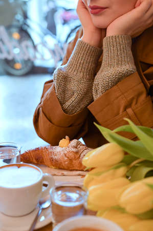 Beautiful young girl in a street cafe with a bouquet of yellow tulips. Breakfast at the coffee shop. Tourism concept. Vintage photo, soft focus. Copy space . close-upの写真素材